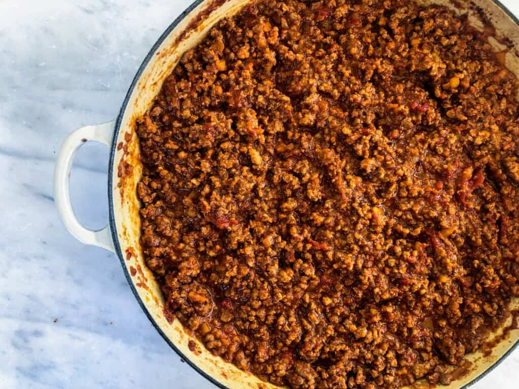 Top view of ragu bolognese in a pot on a white surface.