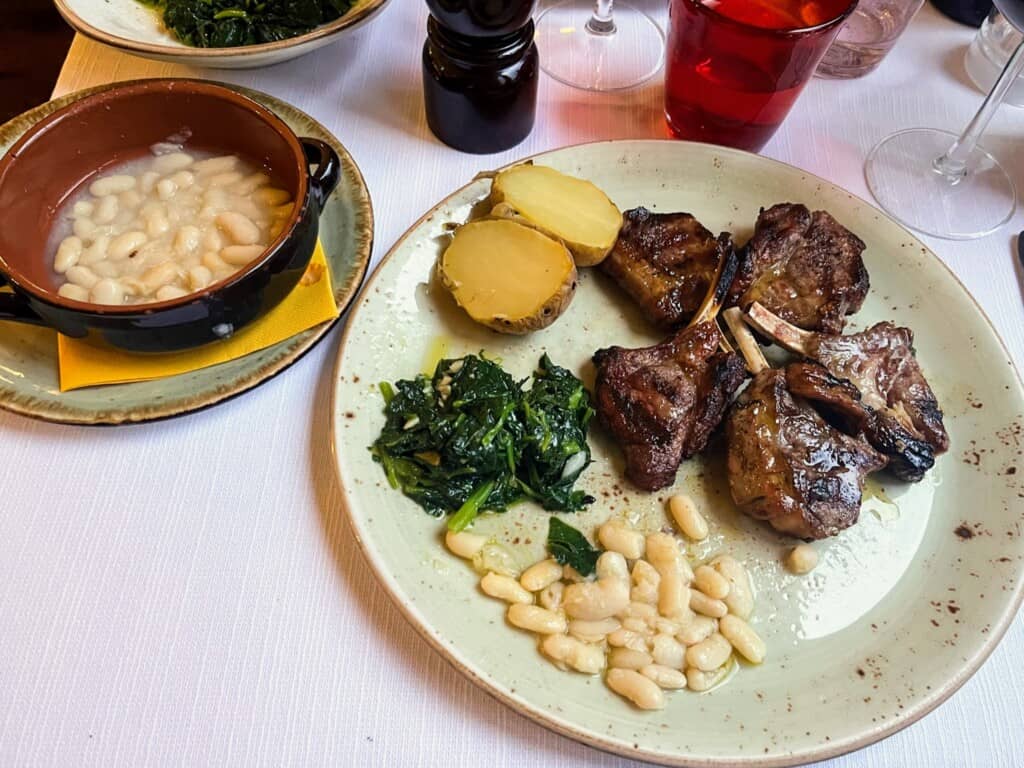 Dinner table with plate of lamb, potatoes, spinach, and beans.