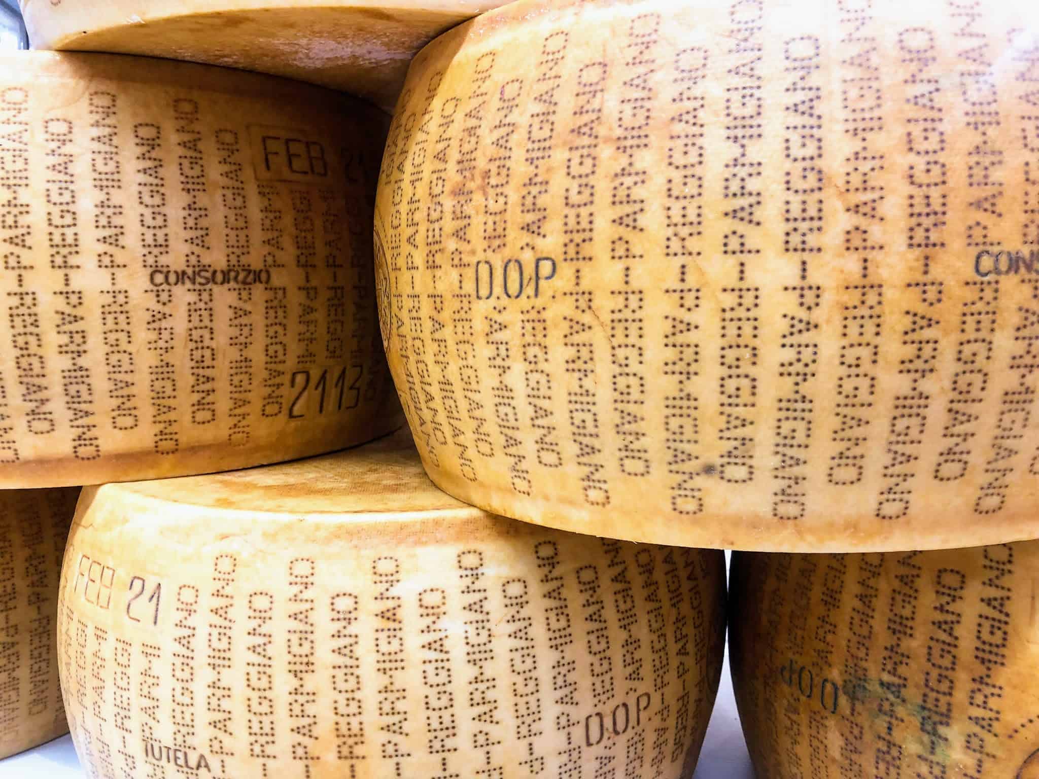 Close up of stacked large wheels of parmigiano reggiano cheese.