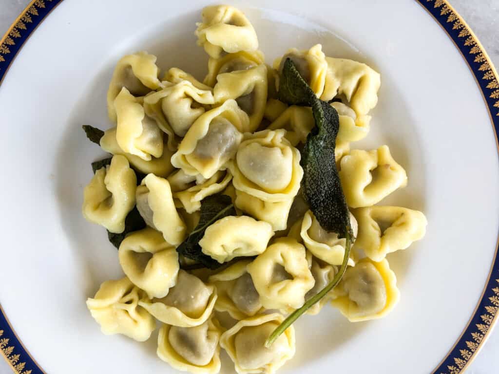 close up top view of tortellini dressed in butter and sage sauce on white plate