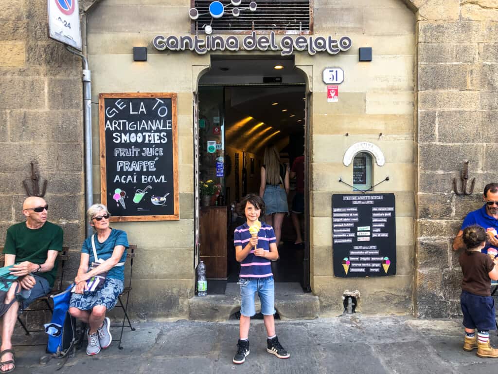 BOY holding a gelato outside an entrance to a gelateria with signs on either side from street view