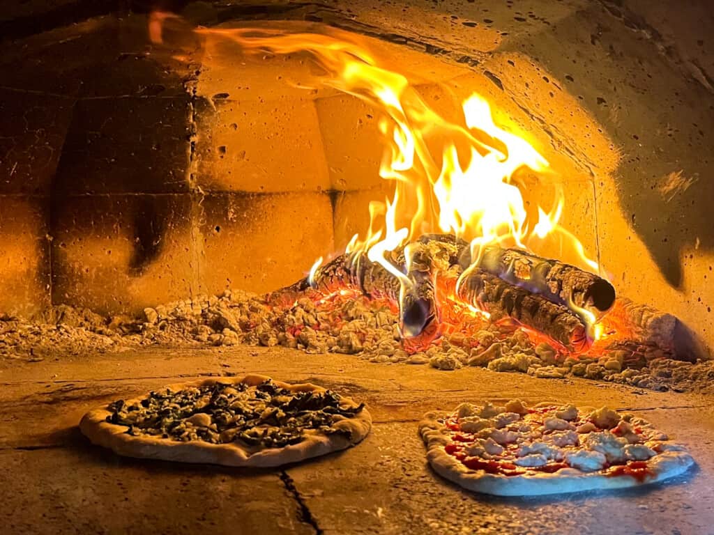 two pizzas cooking in a wood-fire oven from side view