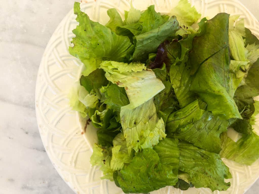 close up top view of white plate on marble board filled with green salad