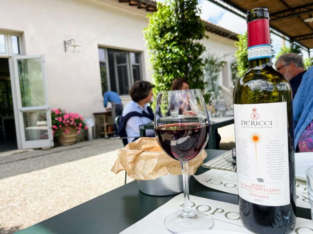 Red wine glass and bottle on a table at a restaurant outdoors in Italy.
