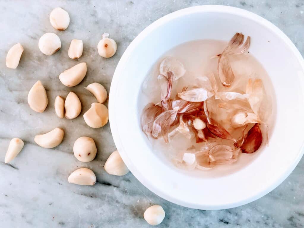 Bowl of garlic peels next to peeled garlic cloves