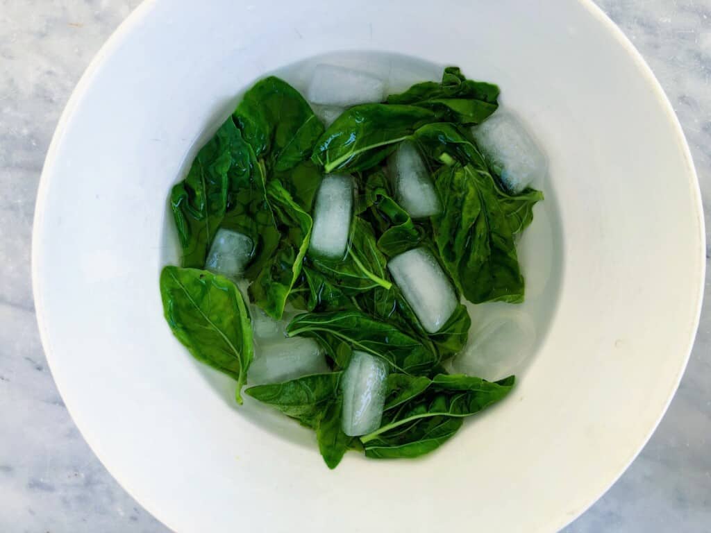 Blanched basil in shallow white bowl with ice cubes