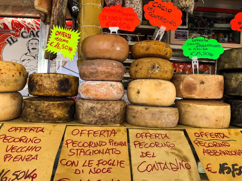 side view of a truck with various pecorino cheese for sale stacked on top of each other with yellow signs indicating type and price in red writing on bottom.