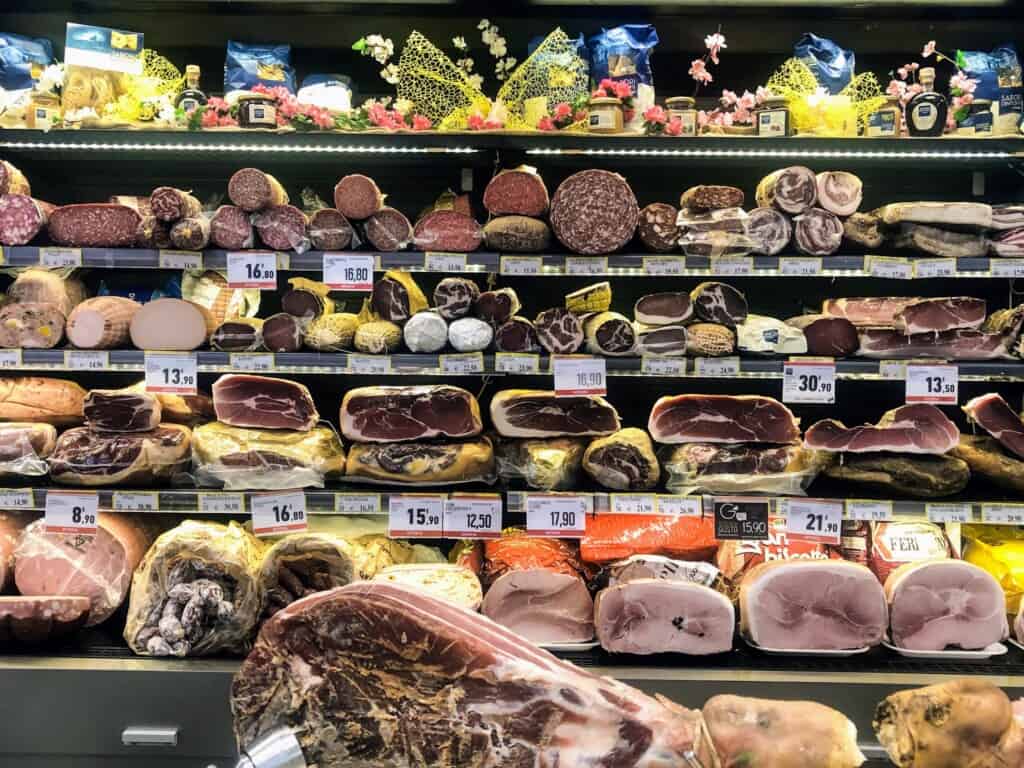 Prosciutto and cured meats on display at a deli in a grocery store in Italy.