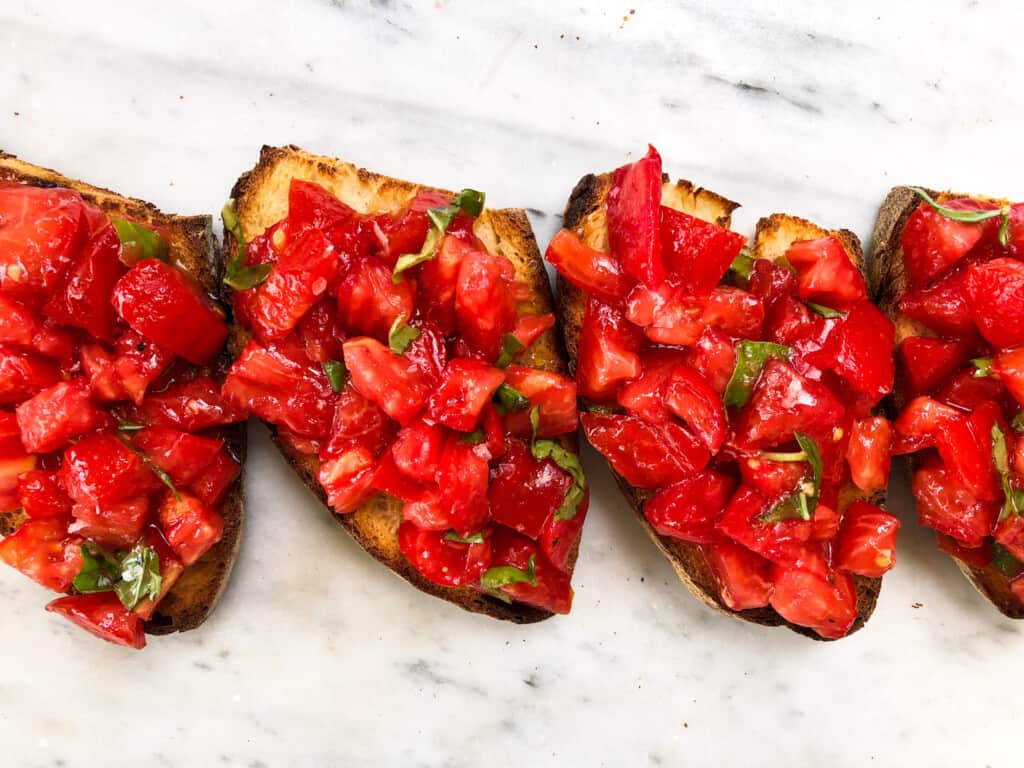 Four slices of toasted bread topped with tomatoes and basil - Italian bruschetta.