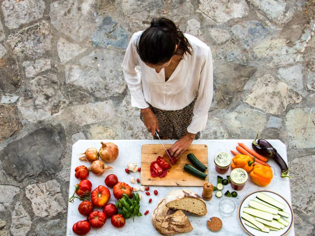 top view of woman standing over a marble table with various ingredients chopping vegetables on a stone floor