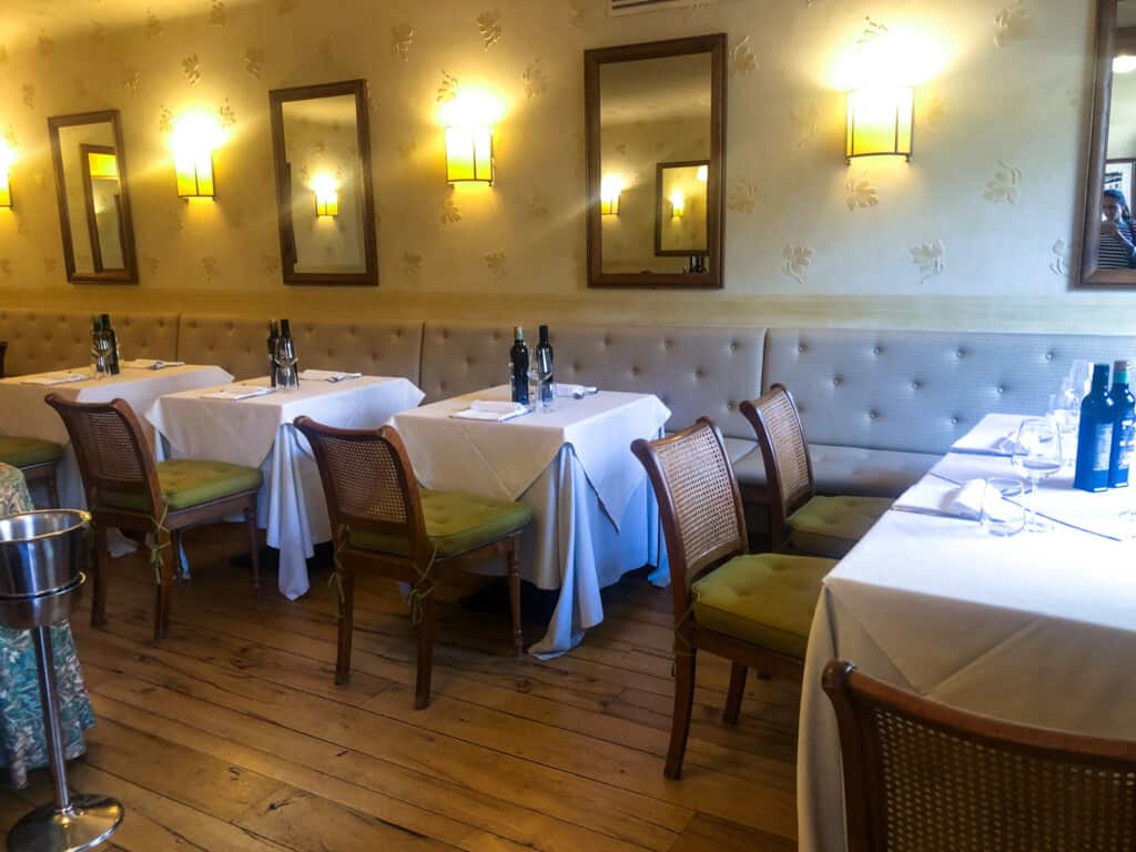Dining area inside Ristorante da Nilo in Cetona. Booth seating and tables and chairs. White tablecloths on each tables, with napkins, silverware, and oil/vinegar bottles.