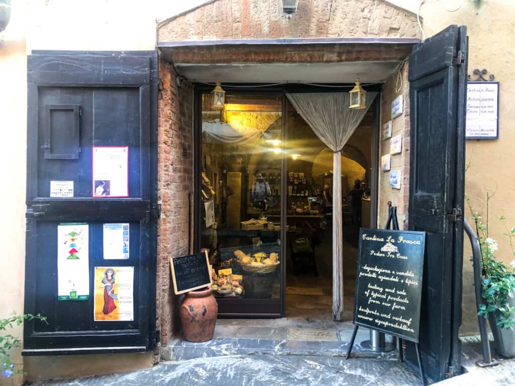 Front entrance of Cantina la Frasca in Cetona, Italy. You can see food and wine products inside on display shelves and in baskets.