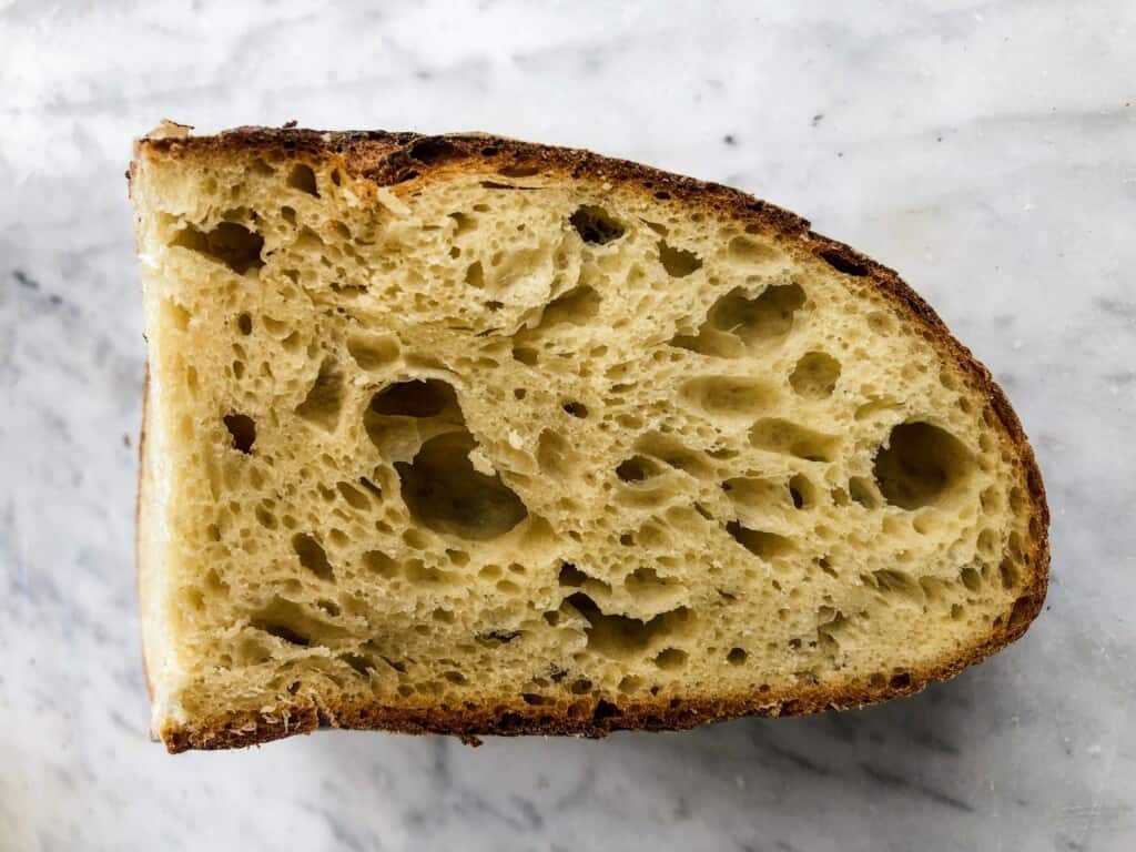 Close up of Tuscan bread sliced thickly. You can see the air bubbles and pockets. It's sitting on a white marble surface.