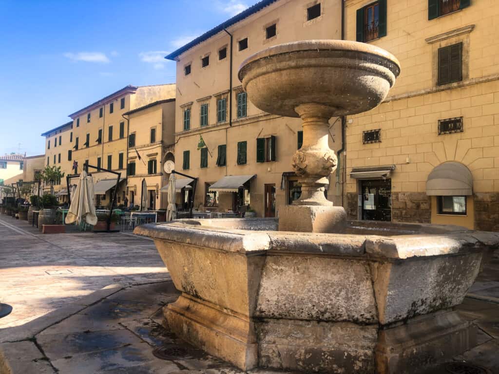 Close up of stone fountain in an Italian piazza. You can see yellow buildings in the background.