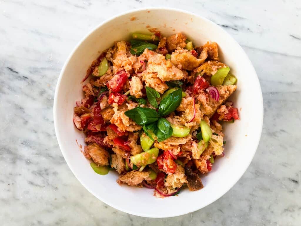 White bowl full of fresh panzanella - an Italian bread salad. It's sitting on a white marble surface.