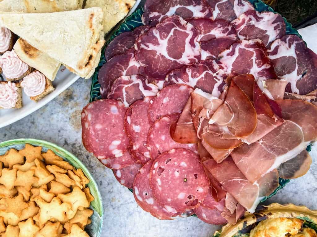 Top view of platter of cured meats, bowl of star-shaped crackers, and other Italian finger foods.