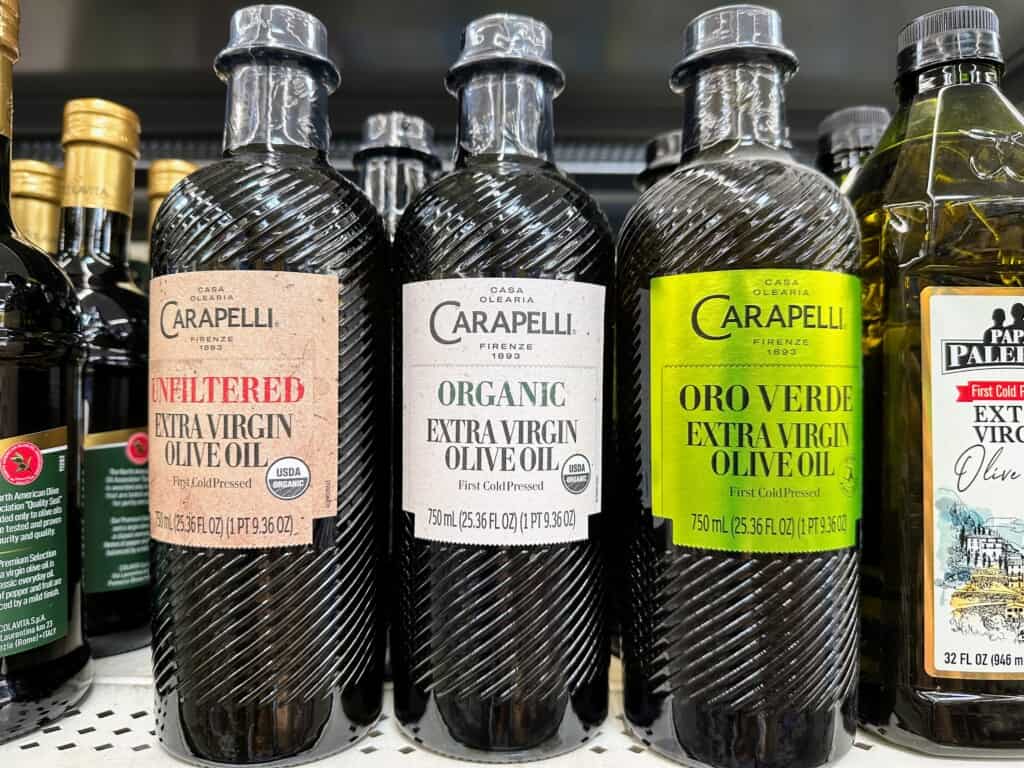 Bottles of Carapelli brand olive oil on grocery store shelf.