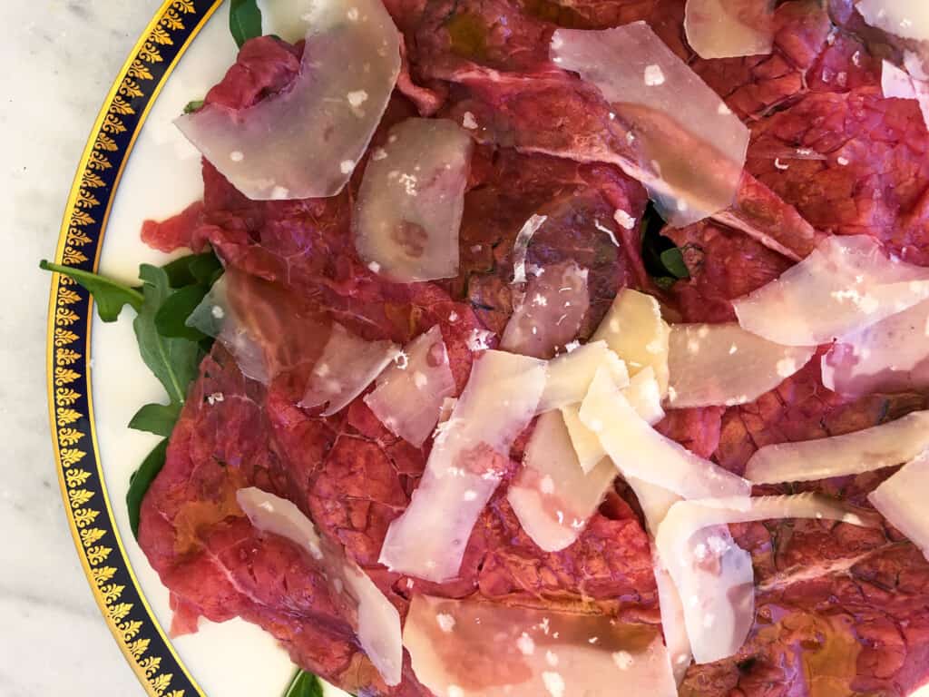 close up of beef carpaccio garnished with parmesan cheese and rocket or arugula.