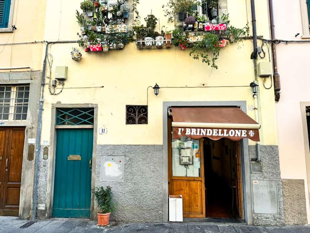 side view of restaurant with a green door and a wooden door with an overhand with written the name of restaurant on a yellow wall from street view