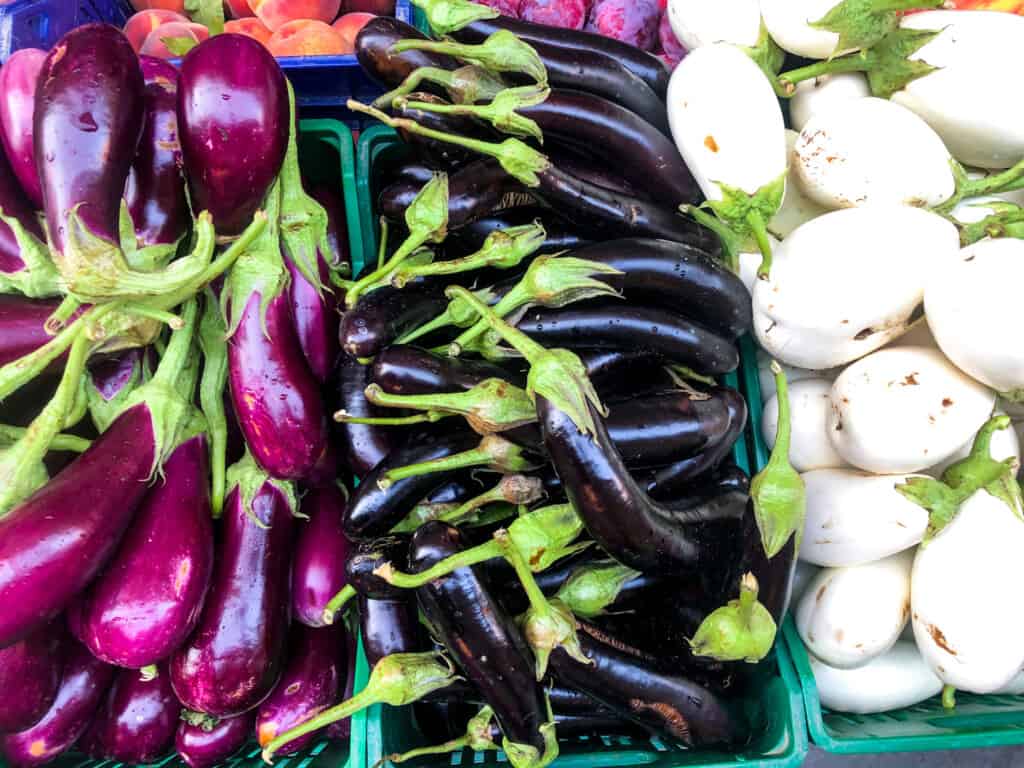side view of several green crates full of different colored eggplants from top view outside at a market in Italy.