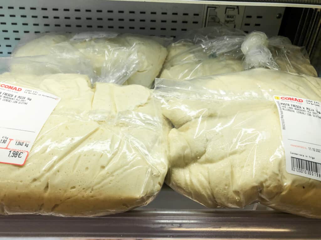 Plastic bags filled with fresh pizza dough on sale at a grocery store in Italy.