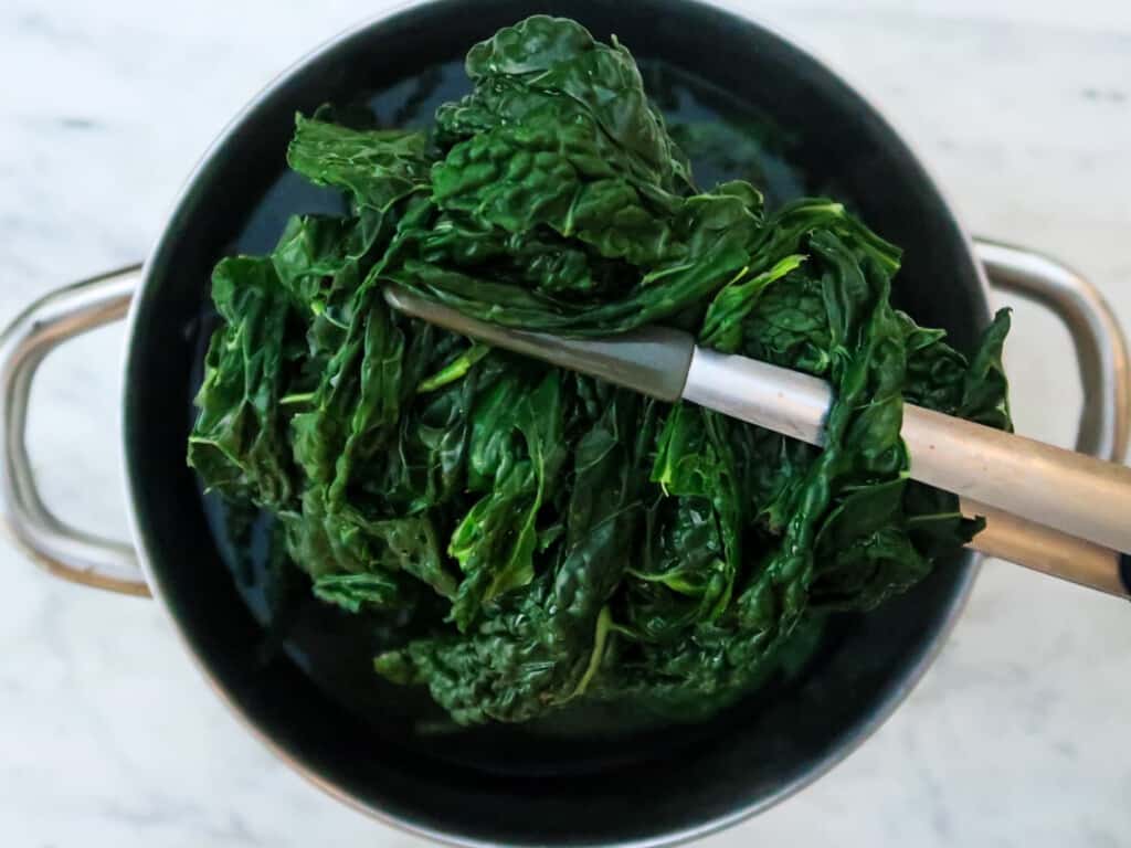Kitchen utensil holds cooked cavolo nero above pot of water.