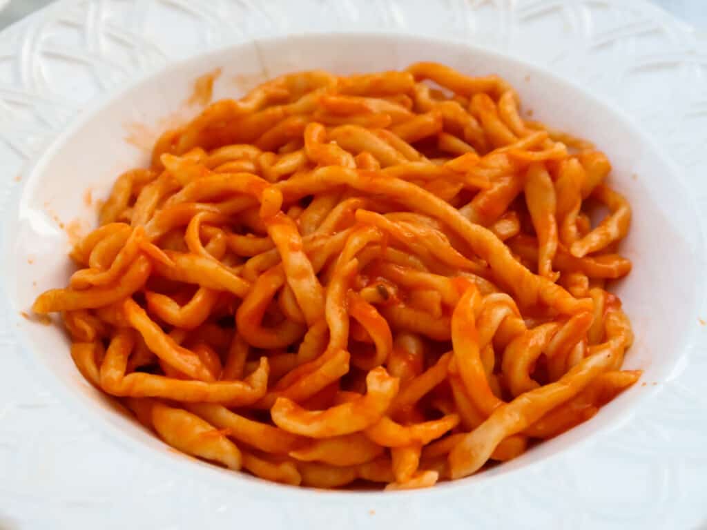 Plate of pici pasta with aglione sauce in a white dish.