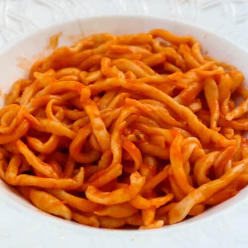 Plate of pici pasta with aglione sauce in a white dish.