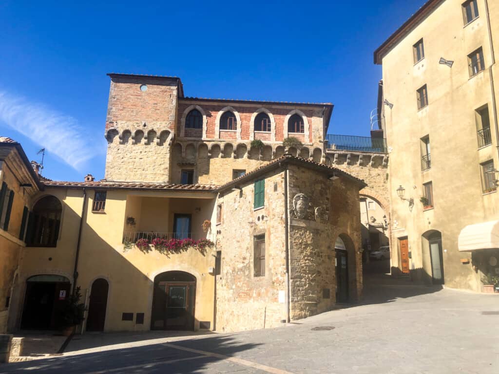 Small square in an Italian village. It's surrounded by stone and brick buildings. No one is in the square.