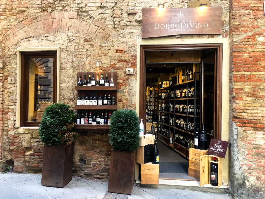 Entrance to an enoteca in Montepulciano, Italy. You can see displays of wine bottles inside the doorway and there are also wine bottles displayed on a shelf to the left of the door, outside.