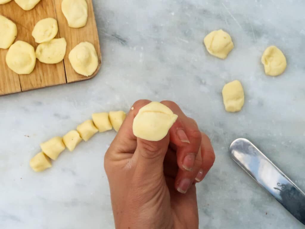 Orecchiette pasta being formed over a thumb. Below on table you see finished orecchiette pasta and some dough.