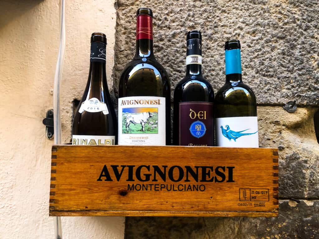 Bottles of wine in wooden box shelf on stone wall.