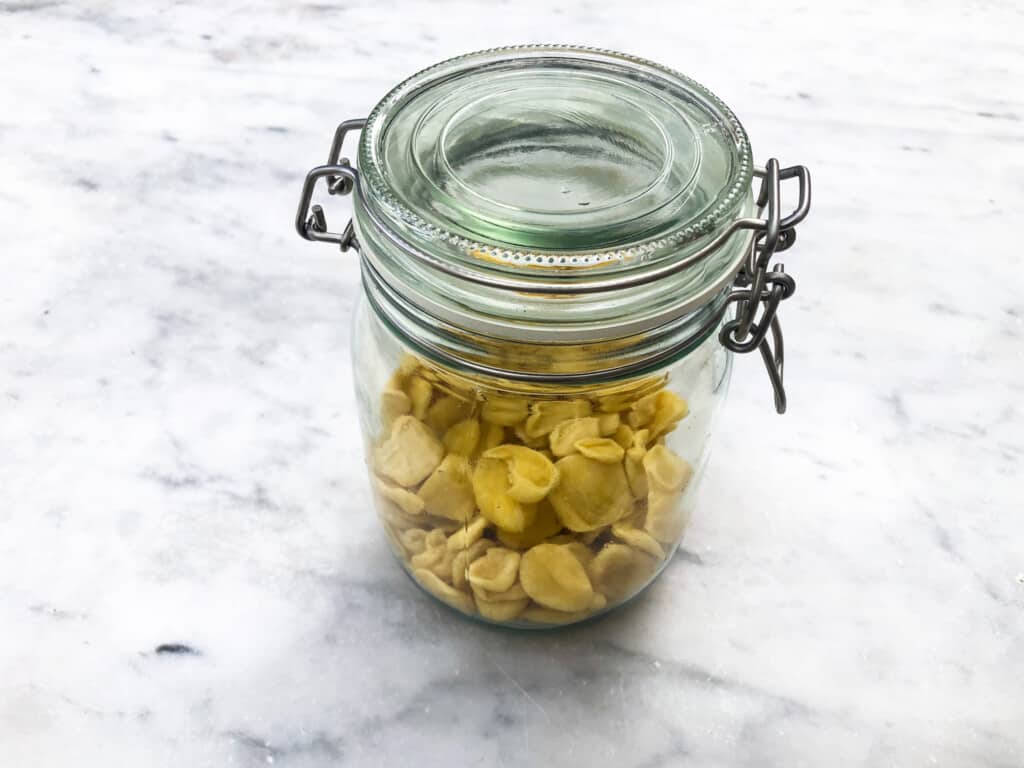 Glass jar full of orecchiette pasta sitting on a marble surface.