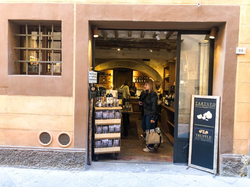 Woman at entrance of truffle shop in Italian village. Displays of truffle products to left of door.