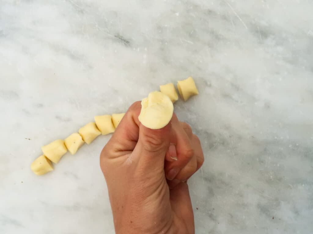 Thumb holding formed orecchiette pasta above cut dough ready to be made into orecchiette.