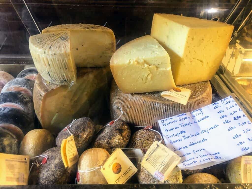Display of whole pieces and chunks of pecorino cheese in a display case along with a handwritten price list.