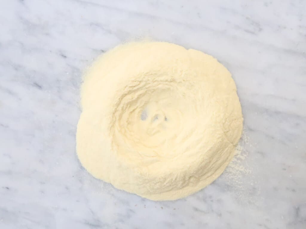 Pile of semolina flour on a white surface with an indent in the middle.