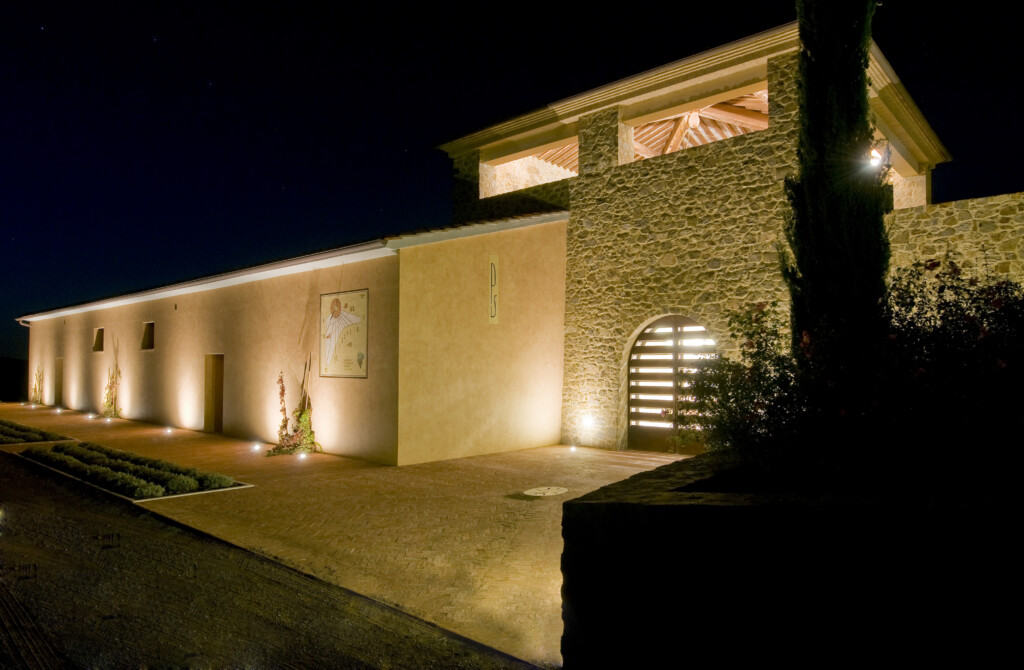 Modern building lit up at night. You can see a sundial on the wall. It's the Azienda Pacenti in Montalcino, Italy.