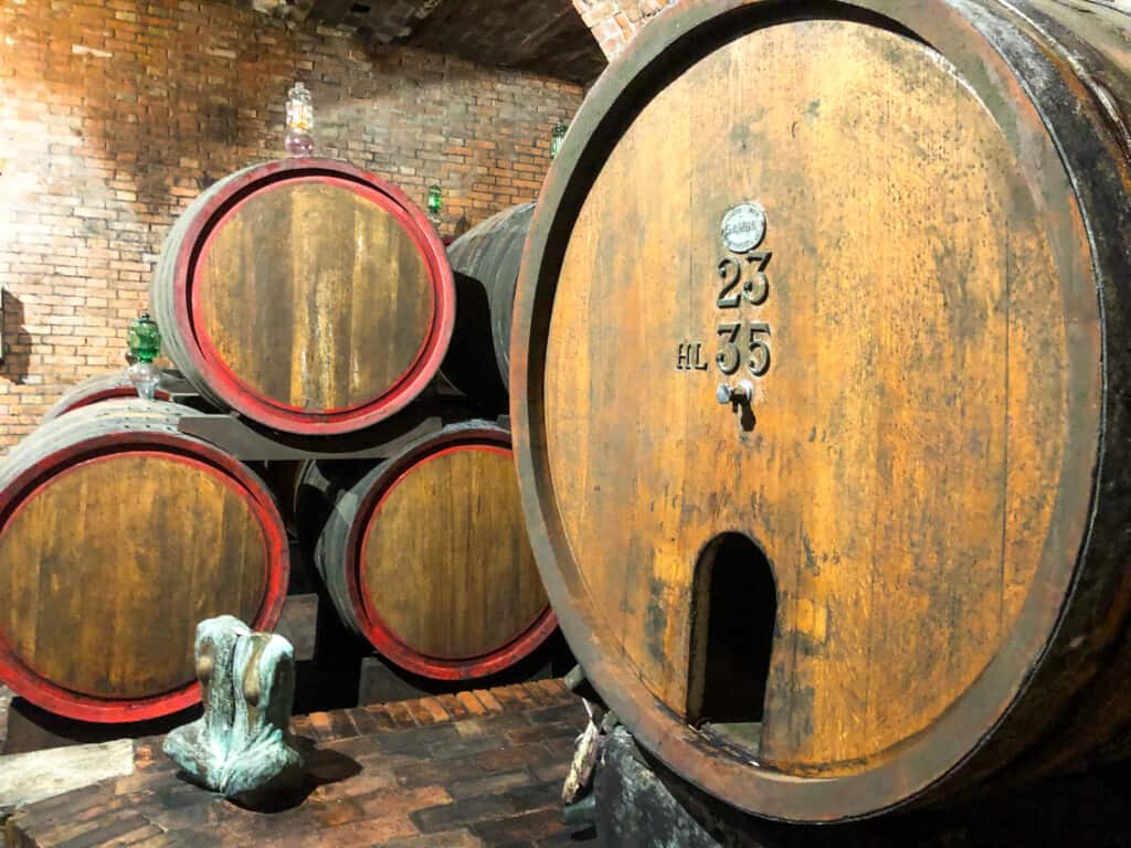 Large wooden barrel next to stacked smaller barrels in an underground winery in Montepulciano, Italy.