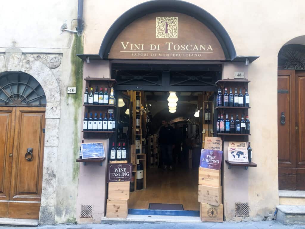 Entrance to Vini di Toscana shop in Montepulciano, Italy. The doorway is arched and there are wines on shelves on either side of the door.