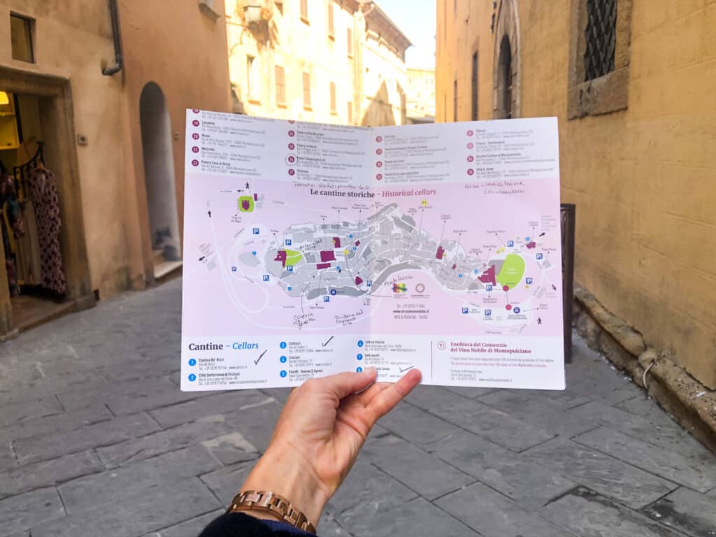 Hand holds up map of Montepulciano's historic cantinas on the street of the town.