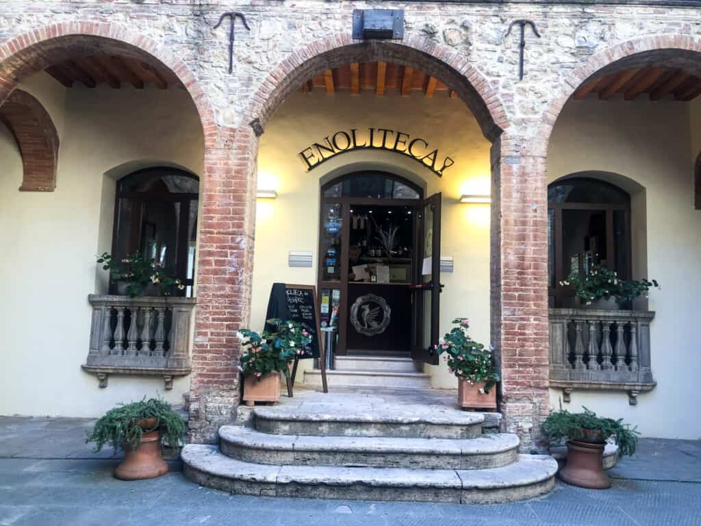 Main entrance to Enoliteca in Montepulciano, Italy. Brick archway in front of door. Chalkboard sign to left of door.