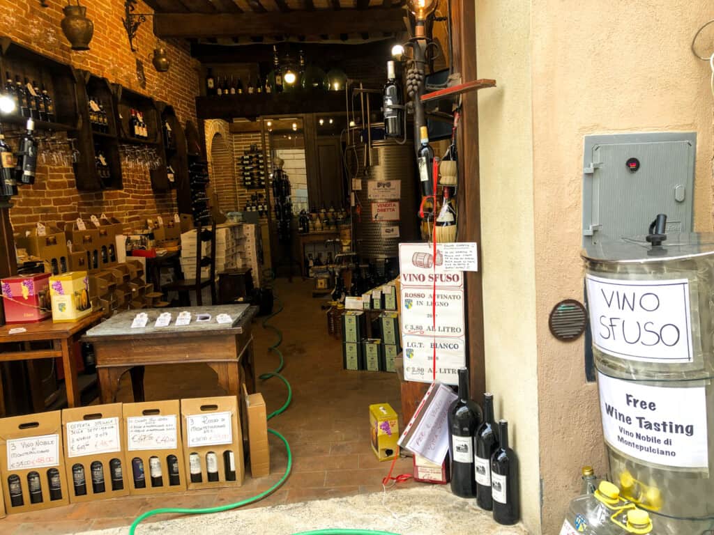 A look inside a vino sfuso shop in Italy. You can see wine bottles on display as well as a large metal wine tank.