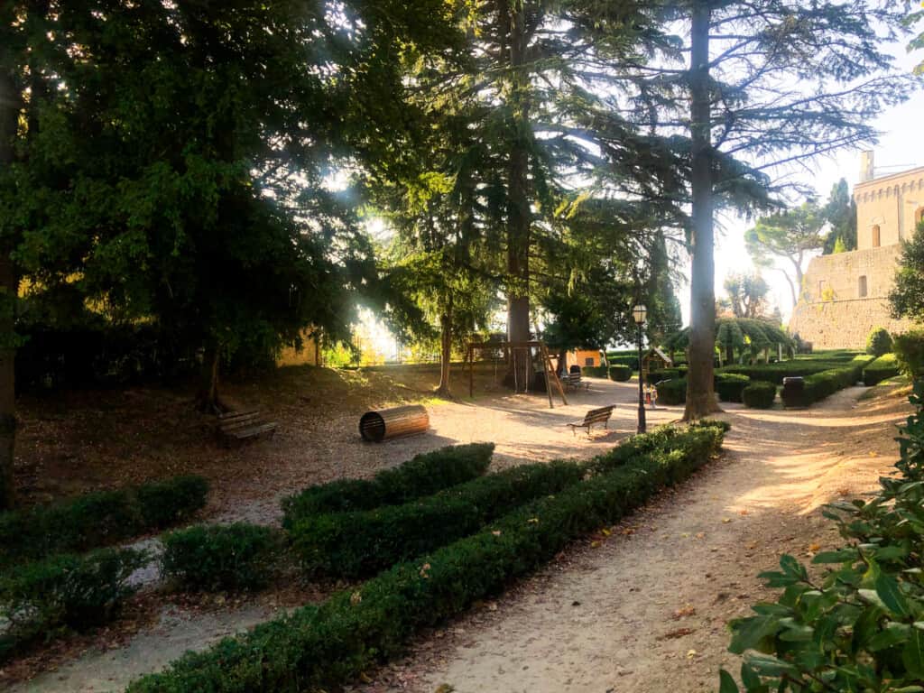 Kids playground shaded by tall trees in Montepulciano. You can see the fortezza in the back right.