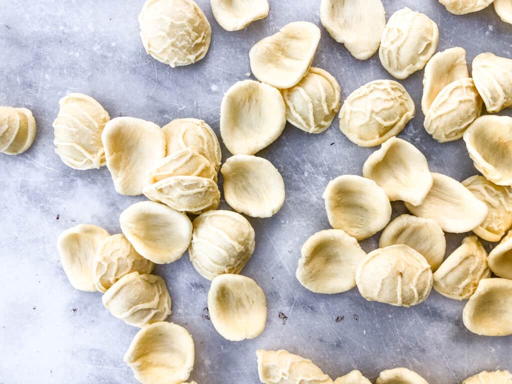 Pile of freshly-made orecchiette pasta on a marble surface.