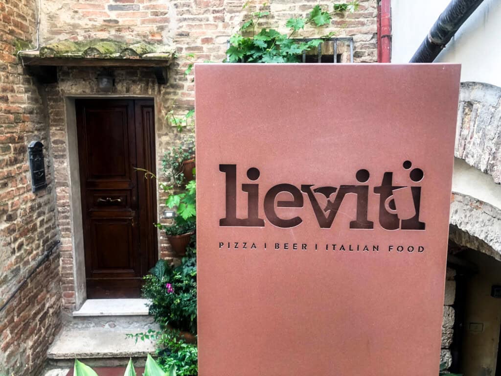 frontal view of a large brown sign with written "lieviti" on the front with a door into a Tuscan brick wall in the background.