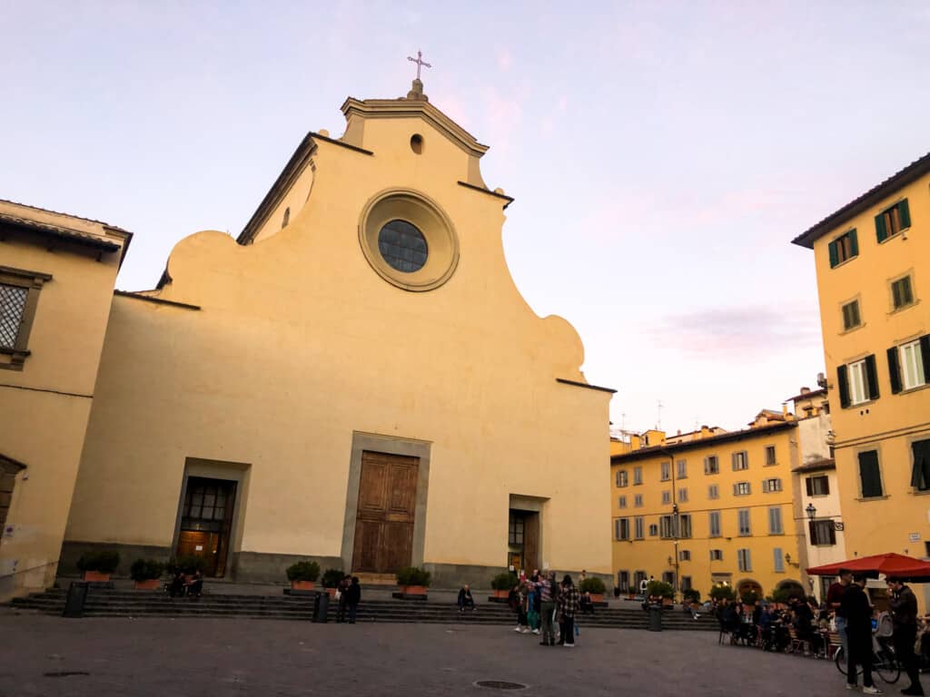 side view of the church at piazza santo spirito with large yellow facade with blue sky in background.