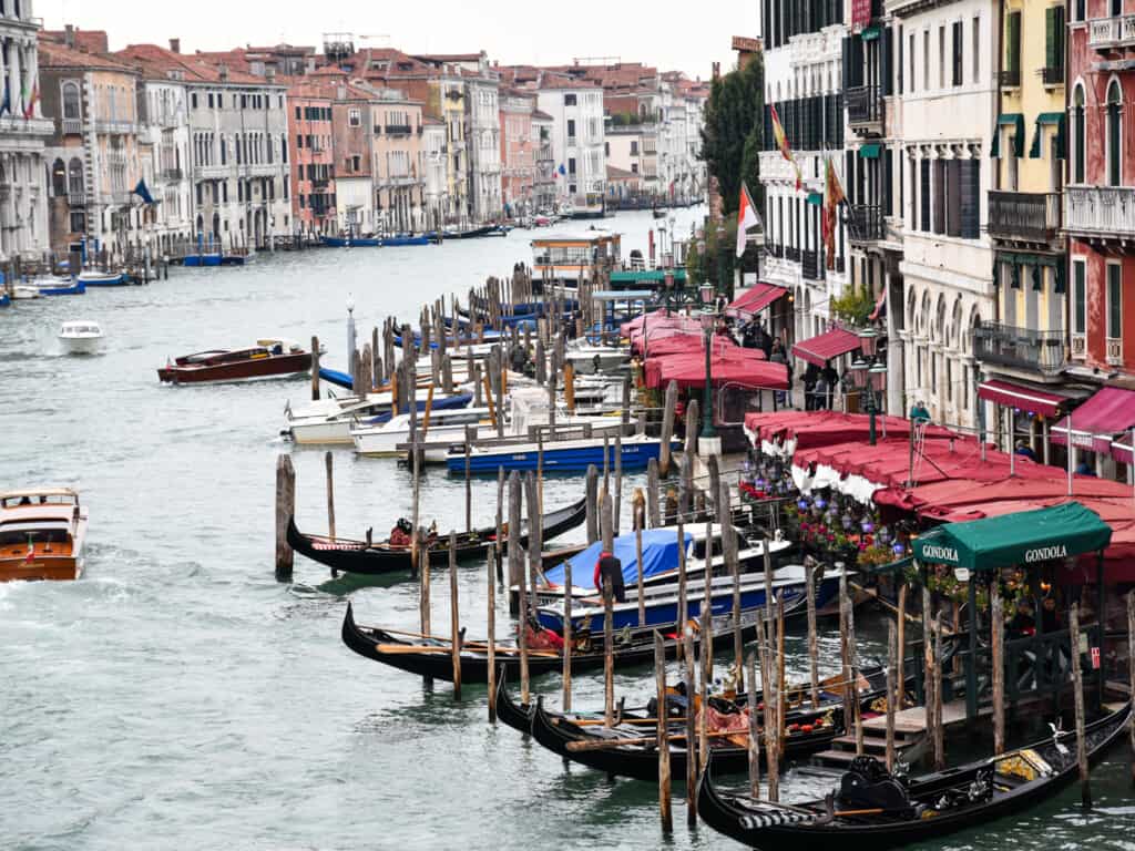 Boats moving down the Grand Canal in Venice, Italy. There are other boats and gondolas docked.