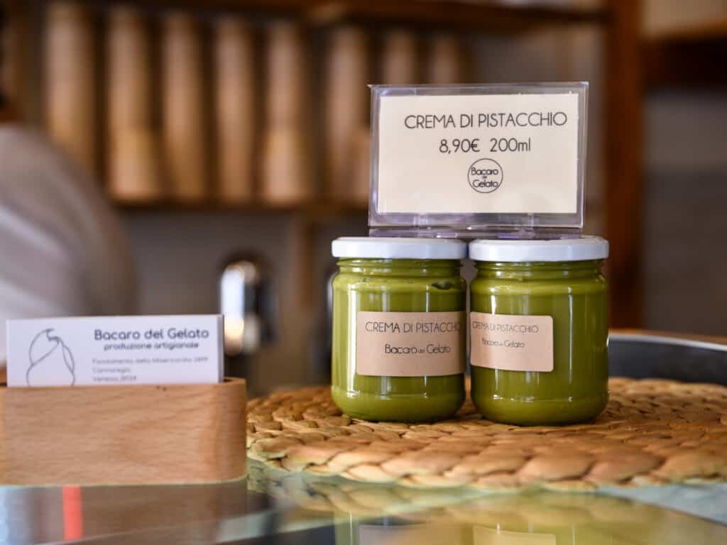 Two jars of pistachio cream with a price sign on a counter in a gelateria in Venice, Italy.