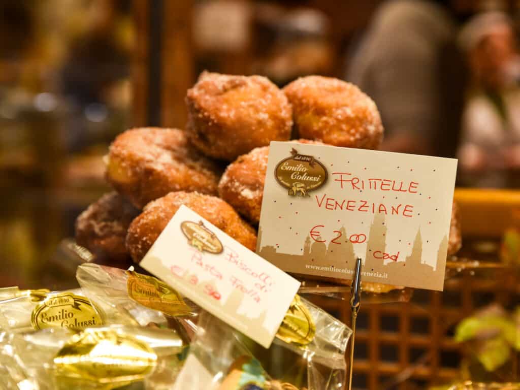 Price tags in front of display of frittelle in Venice, Italy pastry shop.